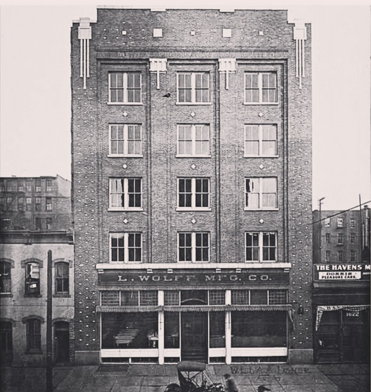 Vintage brick building facade with rows of windows and a storefront sign reading L WOLF MFG CO