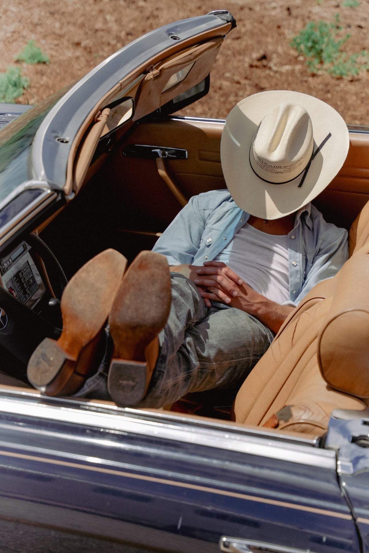 Cowboy shirt and vintage hat on a man sitting in an open car, outdoors on a dirt road