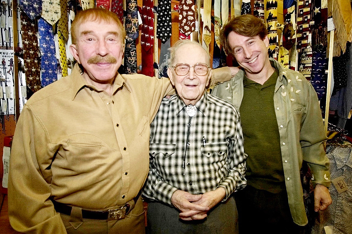 Vintage western wear, two men posing in tan and green shirts with a plaid shirt and store backdrop